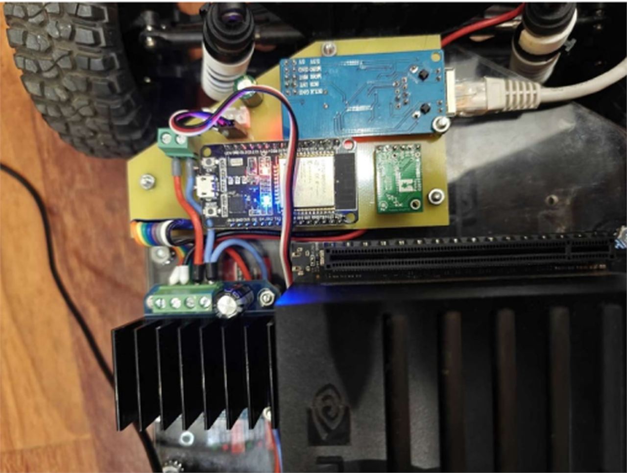 Close-up photograph of the ULSTU control board mounted on the robot, showing a blue W5500 Ethernet module with an RJ45 jack and a grey patch cable plugged into it, an ESP32 development board with a lit blue LED, a small green sensor module, green screw terminals and a black finned heatsink below