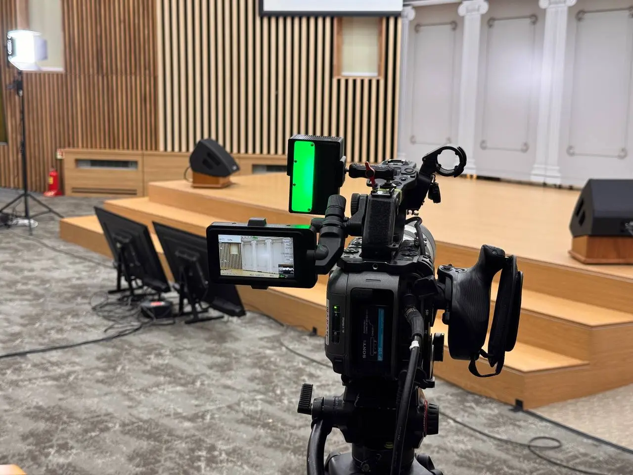 A green TALLY-NODE receiver mounted on a camera in a venue