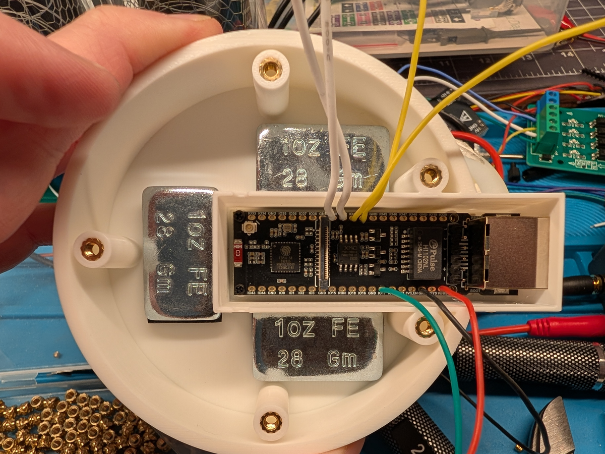 Photograph looking down into the printed base: the ESP32-S3-ETH board sits in a rectangular side pod with its RJ45 jack facing out, steel ballast weights around it, and white, yellow, green, red and black wires soldered to the header