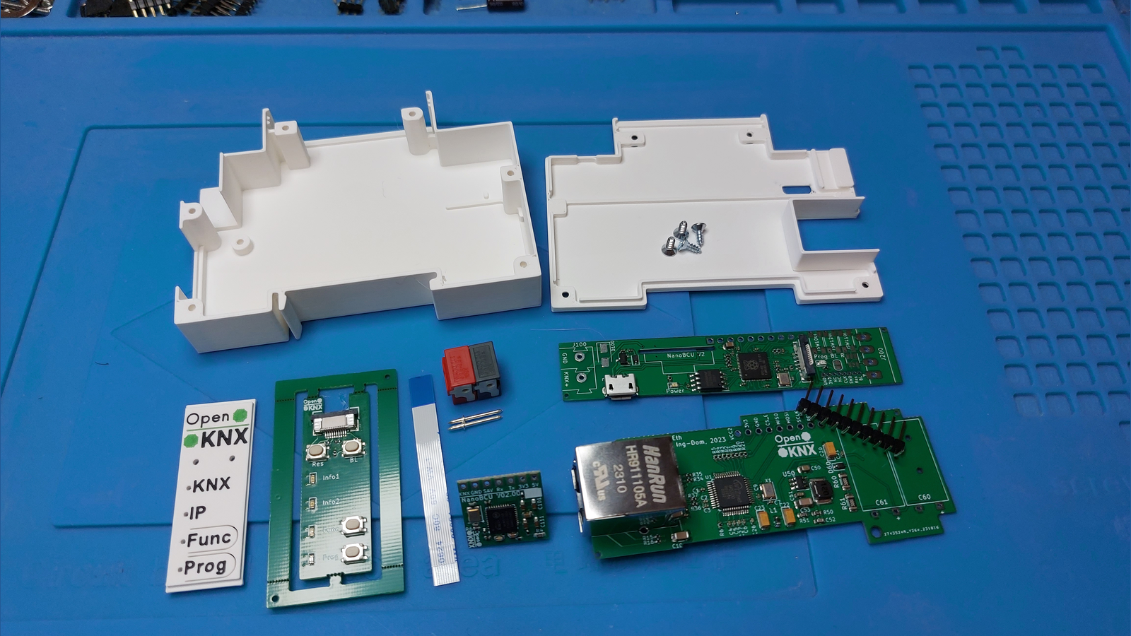 Flat lay of the parts that make up an OpenKNX REG1 LAN Gateway kit, including two white 3D printed case halves, a front panel PCB, a controller board with micro USB, and a green Ethernet application board with an RJ45 jack