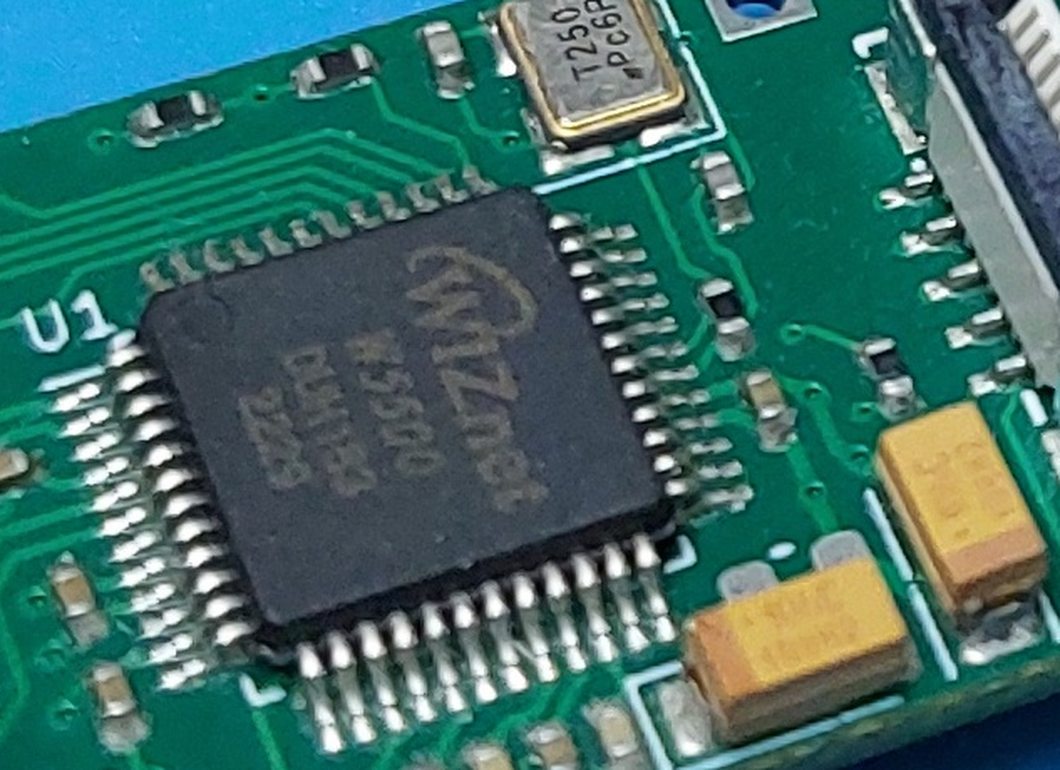 Close macro view of a green PCB showing a black LQFP chip marked with the WIZnet logo and the part number W5500, with reference designator U1 silkscreened beside it and a 25 MHz crystal above