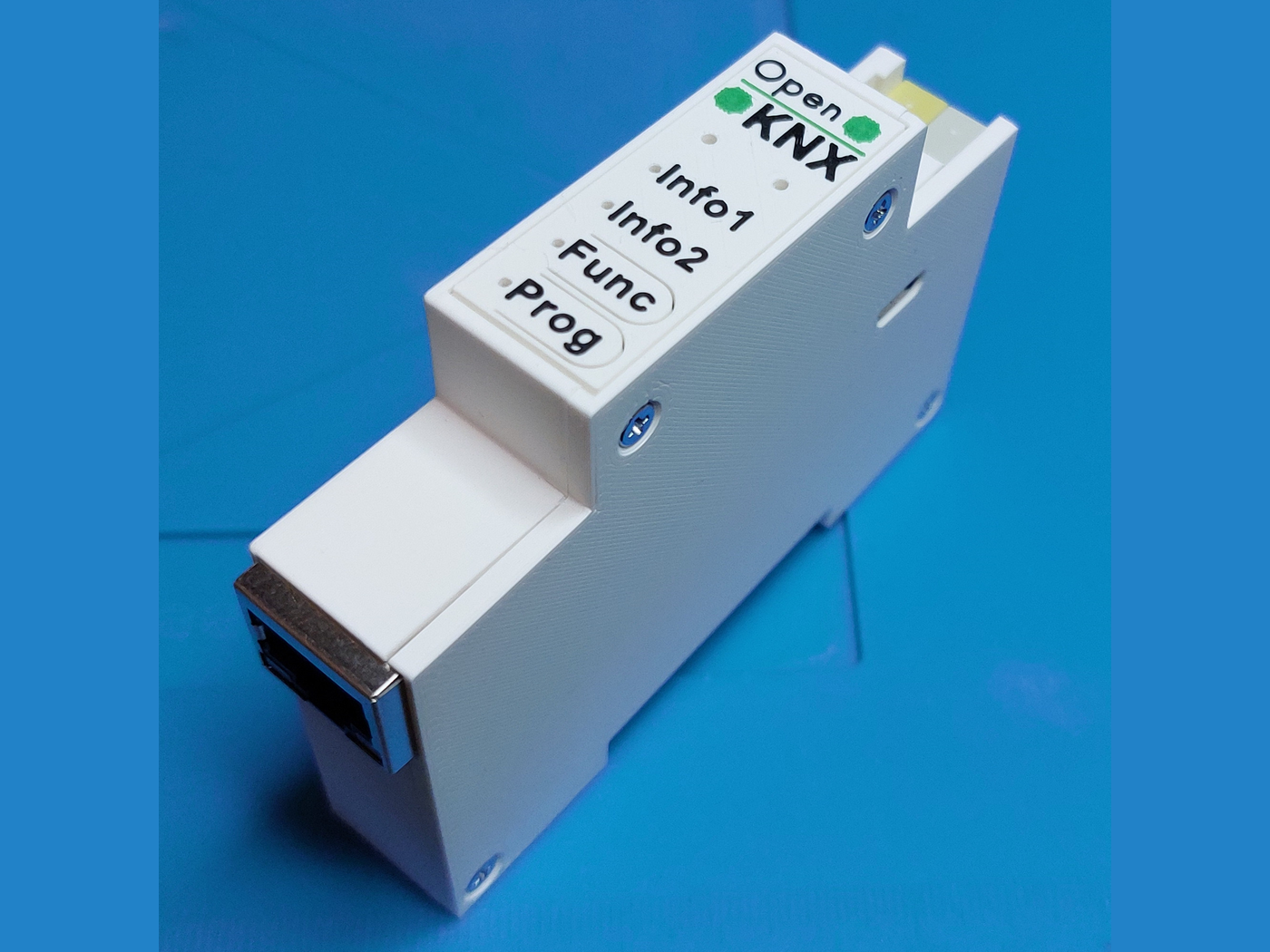 A finished IP-only REG1 device on a blue mat, showing the white 3D printed housing with Info1, Info2, Func and Prog labels on the front and an RJ45 jack on the lower face