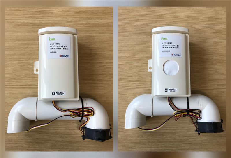 Two white weatherproof sensor units photographed on a wooden desk, each mounting a plastic aspirated duct with a black fan at one end, the left labelled SNTE0001 and the right labelled SNTE0001C with a round white membrane vent