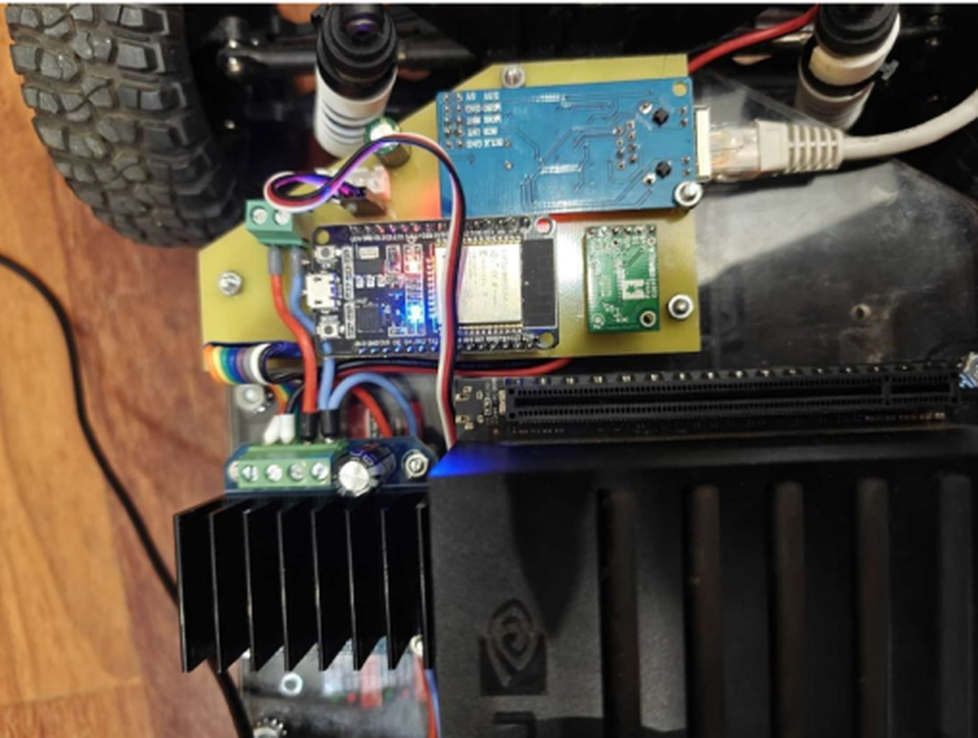 Close-up photograph of the ULSTU control board mounted on the robot, showing a blue W5500 Ethernet module with an RJ45 jack and a grey patch cable plugged into it, an ESP32 development board with a lit blue LED, a small green sensor module, green screw terminals and a black finned heatsink below