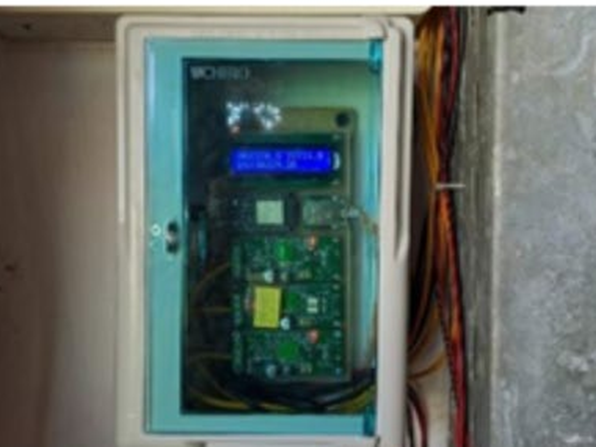 Photo of the deployed monitoring instrument at the BMKG Sleman station, a wall-mounted panel enclosure with a transparent lid showing a blue 16x2 LCD and green circuit boards inside