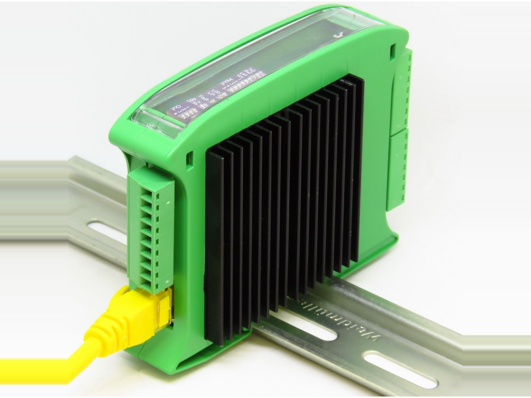 A green DIN-rail mounted GEVINO Motor PLC with a black heatsink and a yellow RJ45 Ethernet cable plugged into the optional network module socket at the lower front