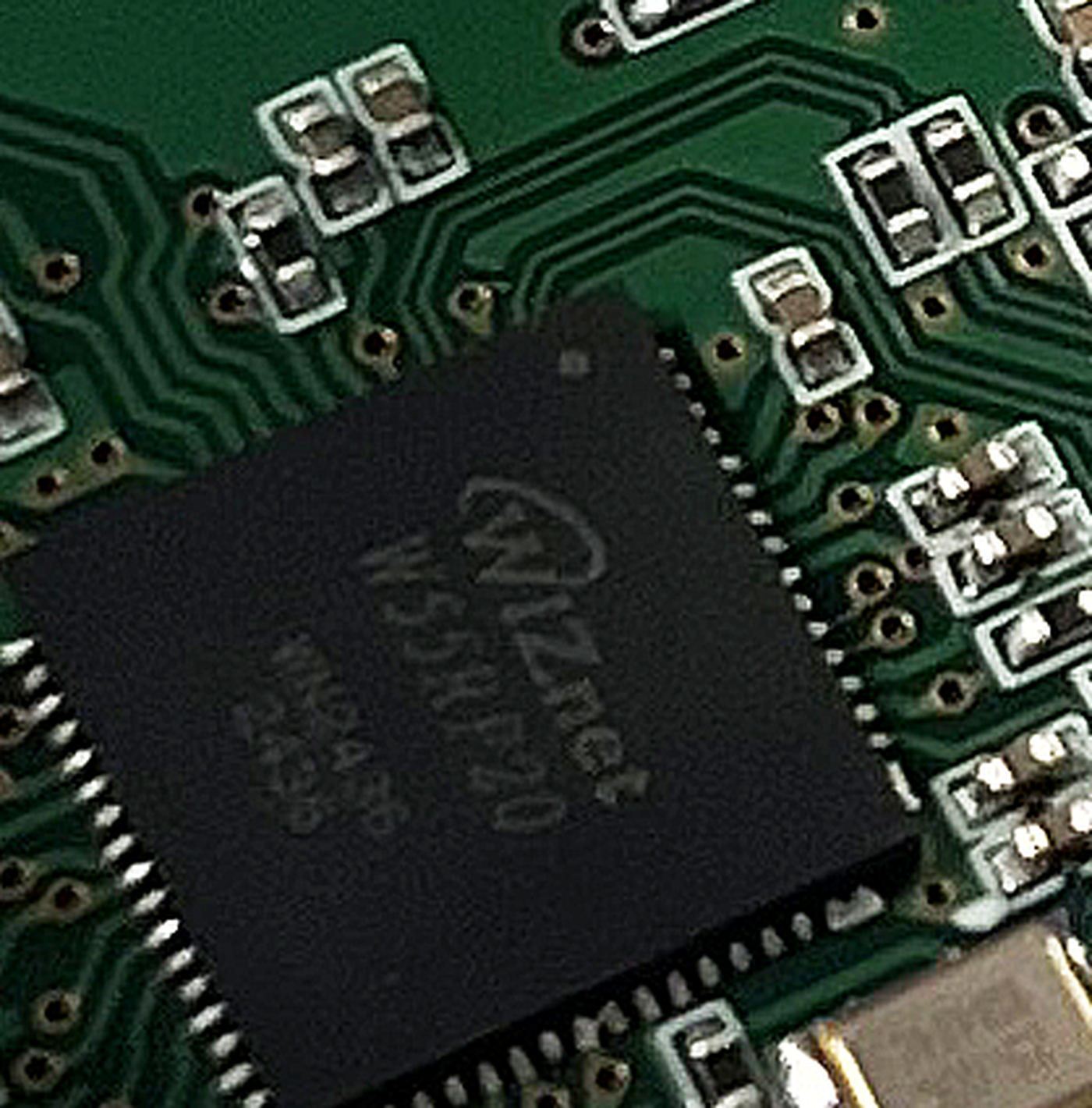 Close macro view of a green circuit board showing a black QFN package laser marked with the WIZnet logo, the text W55RP20 and the date code 2436, surrounded by fine copper traces and small passive components