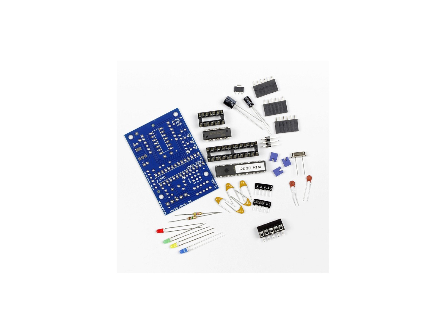 Flat lay of an unassembled Horter I2ARL kit on a white background, showing a bare blue printed circuit board, two DIP integrated circuits with sockets, a black five-pole screw terminal, orange ceramic capacitors, resistor networks, four coloured LEDs, a crystal and three black pin socket strips